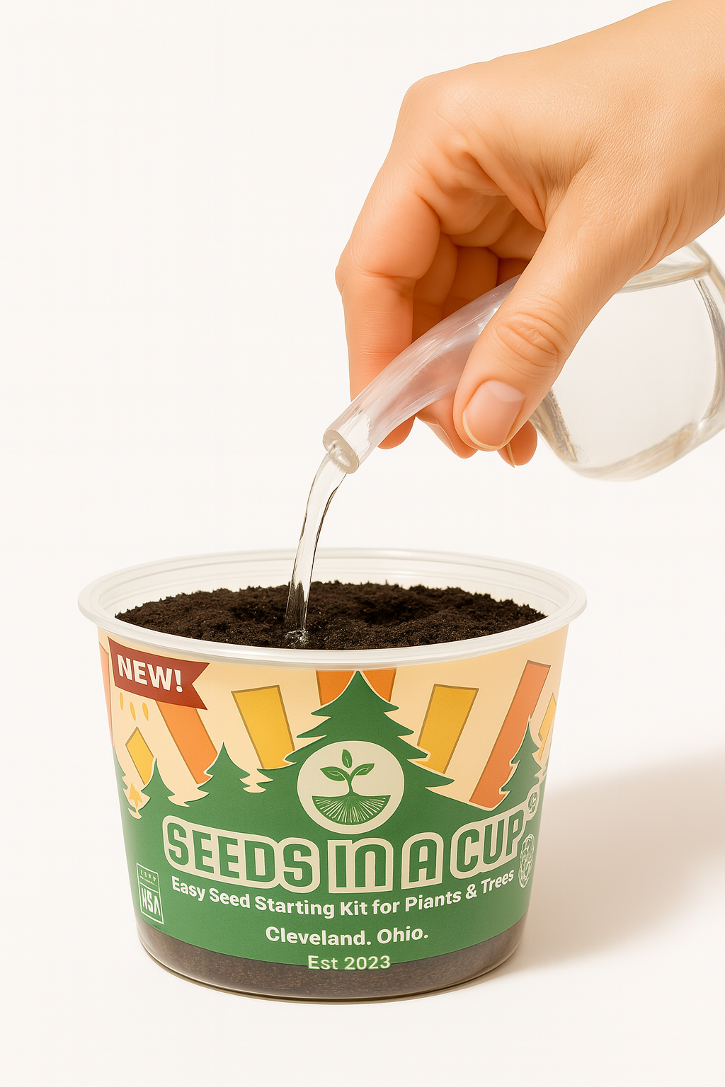 Hand pouring water into a 'Seeds in a Cup' container on a white background how to grow from seed